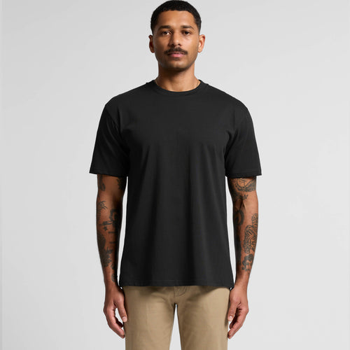 Man wearing a black t-shirt and beige pants on a gray background